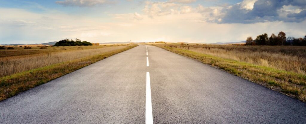 long, empty straight road with open grassland on either side