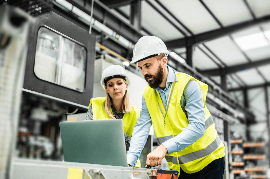 Man and woman in a factory, working on a no-code application, looking at a laptop